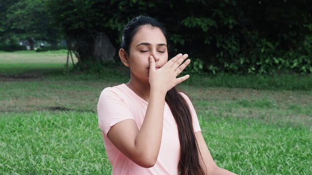 Medium shot of Young girl in sportswear doing nasal or nostril breathing exercise at outdoor - concept of self-care, yoga, workout and healthy lifestyle at outdoors during coronavirus covid-19.