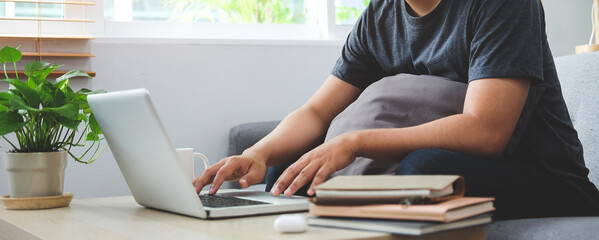 Cropped shot man sitting in living room and using laptop computer.