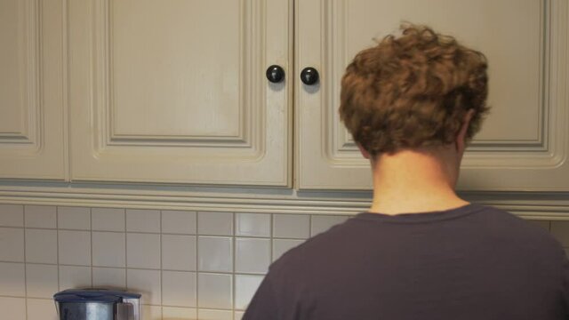 Man in kitchen takes lunchbox from press. MEDIUM SHOT