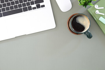 Computer laptop, coffee cup, houseplant and notebook on grey background.