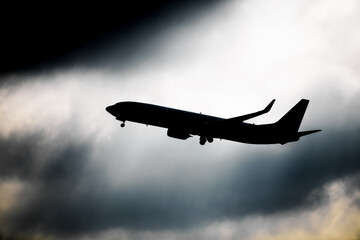 Silhouette of passenger airplane is flying in the cloudy sky