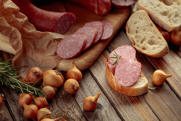 On a old wooden table sausage with bread, rosemary, onion and pepper.
