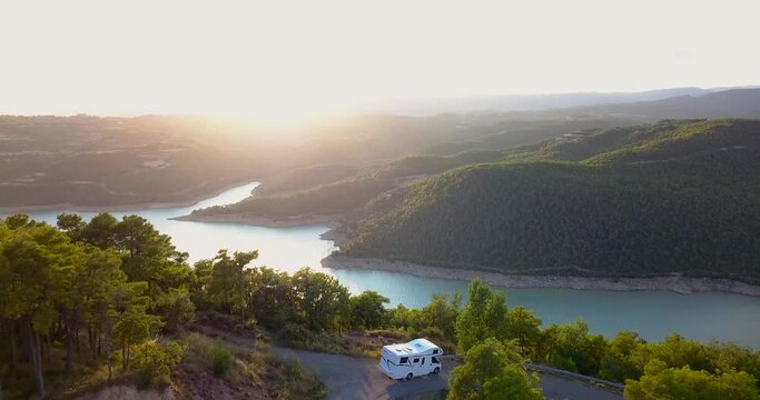 Drone flying forwards revealing a caravan parked with incredible views of a blue and turquoise lake surrounded by dense green forest. 4K aerial footage.