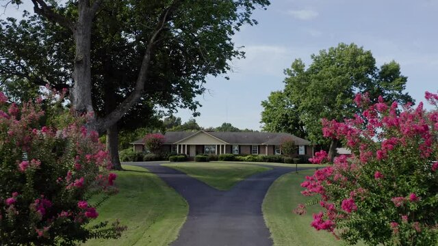 4K aerial pushing in past pink bushes up drive to idyllic southern farmhouse