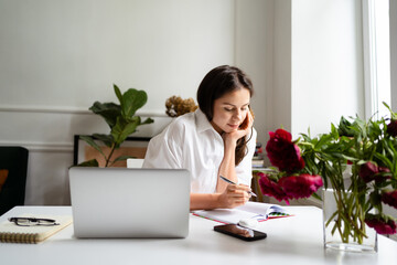 Image of young cheery positive beautiful business woman sitting indoors in office or home office using laptop computer.