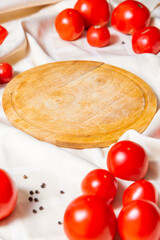 Wooden round cutting board surrounded by tomatoes.