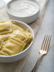 Serving ravioli on a white plate and fork. In the background is a bowl of sour cream. White napkin. Light background. Close-up. Restaurant, hotel, cafe, home cooking.
