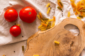Ingredients for cooking: three tomatoes, a fragment of an uneven cutting board, pasta, pepper.