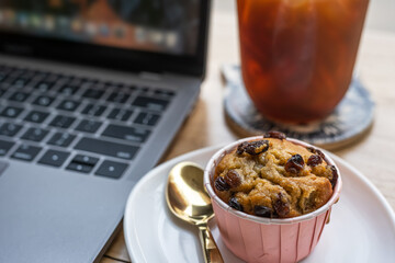 Close-up of ice coffee in cup mug and Homemade Banana cup cake with keyboard laptop computer on wood desk office desk in coffee shop at the cafe,during business work concept