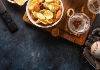 Light beer in a glass, potato chips on a wooden tray. Dark blue background. High angle view. Watching your favorite TV shows and sports matches with friends. Rest, relaxation.
