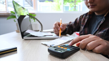 Close up of Asian man using calculator and managing household finances at home.