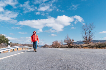 A man walking on the asphalt road under a blue sky with some clouds