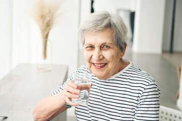 A beautiful elderly woman drinks clean water from a glass.