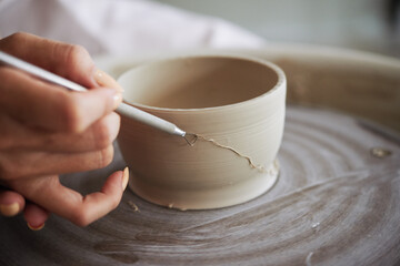 Close-up image of ceramist removing controlled amounts of clay from wheel-thrown clay pot with...