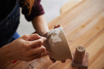 CLose-up image of woman taking off excess clay from the mug she created in pottery studio