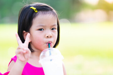 A cute girl is drinking water with a straw. Child showing two finger up as a symbol. On a hot day. Headshot children aged 4-5 years old.