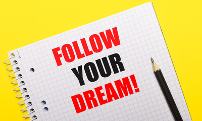 White notebook with inscription FOLLOW YOUR DREAM written in black pencil on a bright yellow background.