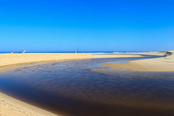 Obraz premium Le courant d'Huchet serpente au milieu du sable de la plage de Moliets dans les Landes pour finir par se jeter dans l'océan. Le ciel est bleu, il fait beau, c'est l'été