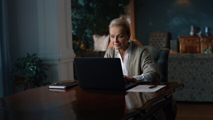 Smiling old woman reading good news on laptop computer at home