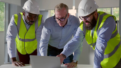 Architects discussing blueprint on laptop with construction manager in office