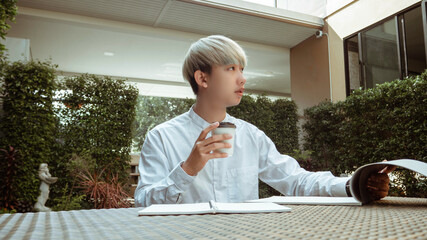 Working outdoor concept a cool young boy holding a cup of hot americano working peacefully in a co-working space of his condominium