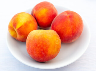 Ripe peaches in a white plate on the table.