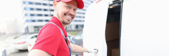 Man courier with delivery receipt and cardboard box in hands opening minivan