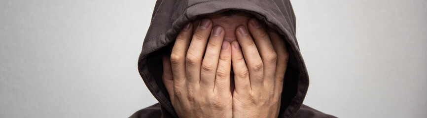 banner of portrait of young adult man in the gray hood covered his face with his hands