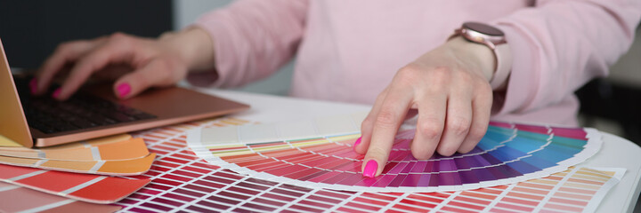 Designer typing on laptop keyboard and choosing color in palette closeup