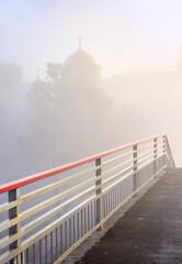 Fototapeta premium Red railings of a pedestrian bridge on the background of a temple in the fog in Novosibirsk