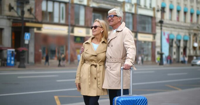 Portrait happy older woman hugging man with suitcase on city street