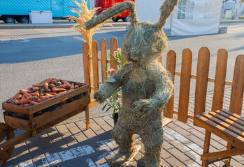 Fairy-tale character straw hare on the background of a wooden fence and wheelbarrows with carrots