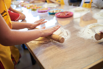 Child wearing yellow apron, making dough on the table. Close-up picture of hands, stretching dough...