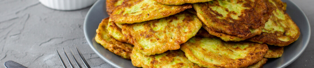 banner of Fritters from zucchini in grey plate with sour cream sauce and greens. Vegetable pancakes of courgettes