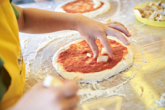 Child wearing yellow apron, putting ingredients dough on the table. Close-up picture of hands, making topping for pizza. Bakery master class for small children. Pizza workshop at juniors' party.