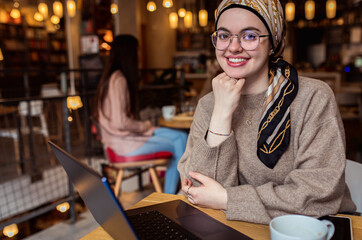 Portrait of young woman working on using laptop at coffee shop.