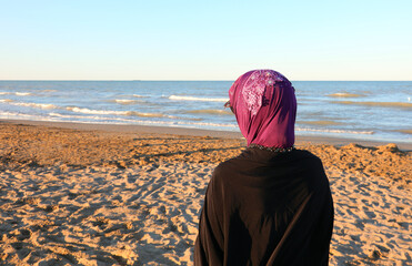 Arab woman with veil on her head waiting on the beach