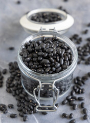 Fototapeta na wymiar Glass jar full of dry black beans on grey table closeup