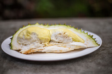Ripe durian with peel is placed on a white plate. Blurred background.
