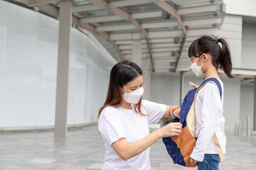 Asian mother helps her daughter wearing a medical mask for protection Covid-19 or coronavirus outbreak prepare to go to school when back to school order.