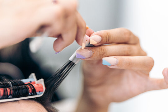 Focus on the painted nails of a hairdresser while curling the hair of a client