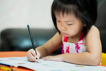 Asian cute kid holding black crayon coloring on book work. Serious girl with homework.