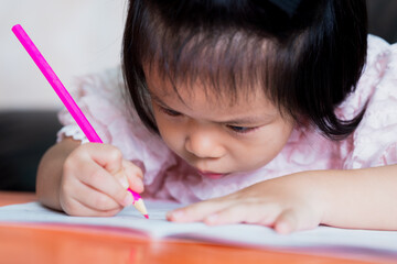 Cute Asian girl is coloring a wood color pink in a book. Child looked down at the close up. Concept of sitting posture and problem with eyes.