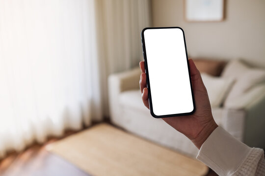 Mockup image of woman holding mobile phone with blank desktop white screen at home