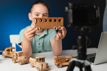 Kid blogger filming video on camera indoors with blue light in background. Online reviewing....