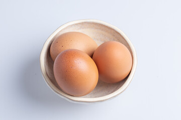 Three fresh eggs in a cup on a white background.