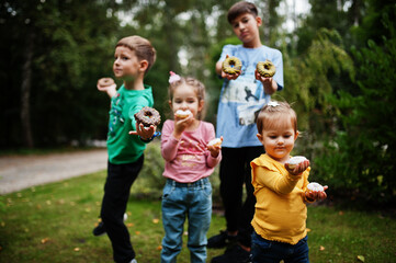 Four kids with doughnuts at evening yard. Tasty yummy donut food.