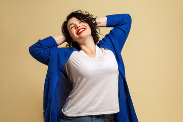 Positive plump girl. Young beautiful brunette in a blue sweater and jeans laughs. Yellow background.