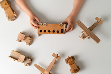 Kid hands playing with wooden toys, bus, plane, cars on white background with blank space for text. Top view, flat lay.