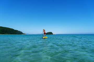 Tanned man relaxing sitting on surfboard with paddle relaxing at coast summer travel vacation